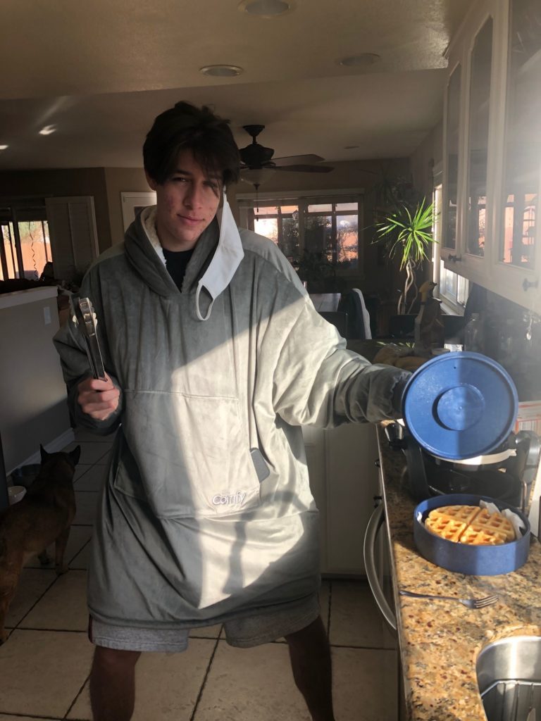 A young man cooking waffles. Eating at home can be cost effective and fun! Make food prep a time to connect!