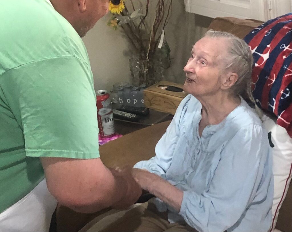 Picture of a young man holding the hand of a happy elderly woman.  time talking to elderly can be a random act of kindness that boosts well-being